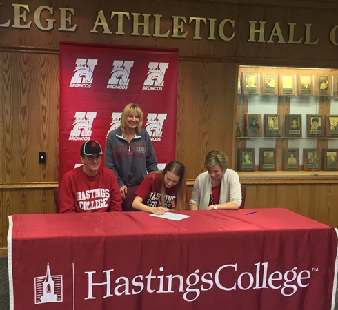 Marshfield Columbus Catholic High School senior Jessica Trad, seated in the middle, signed a letter of intent to play basketball at Hastings College in Hastings, Neb., last weekend. Trad’s father, Dr. Michael Trad, is to her left, and Hastings coach Jina Johansen is to her right. Trad’s mother, Suzan Trad, is standings. (Submitted photo from Trad Family)